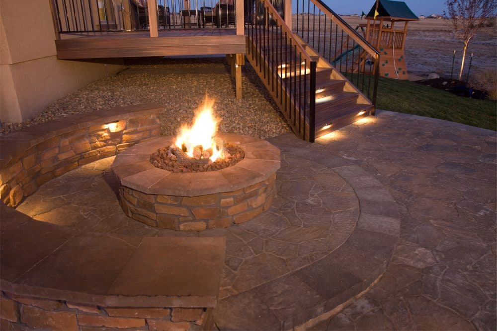 A stone fire pit with step lighting in the background