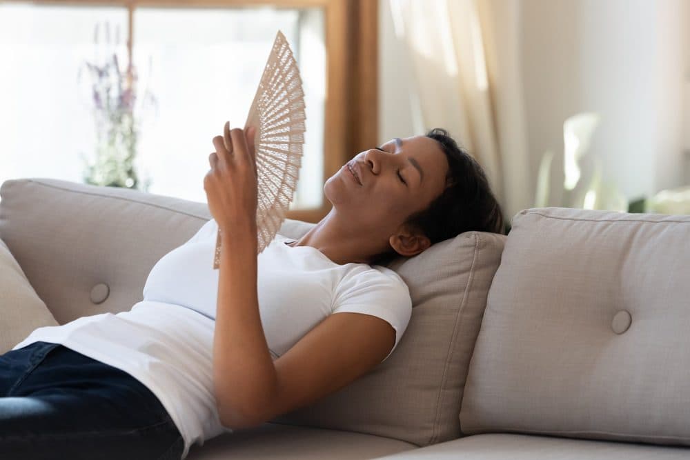 A woman laying on her couch using a handheld fan to keep herself cool