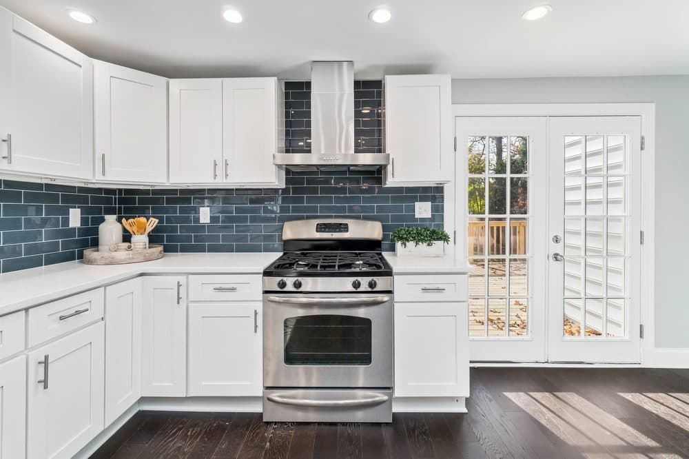 Recessed lighting inside of a kitchen with white cabinets, stainless steel appliances, and blue subway tile