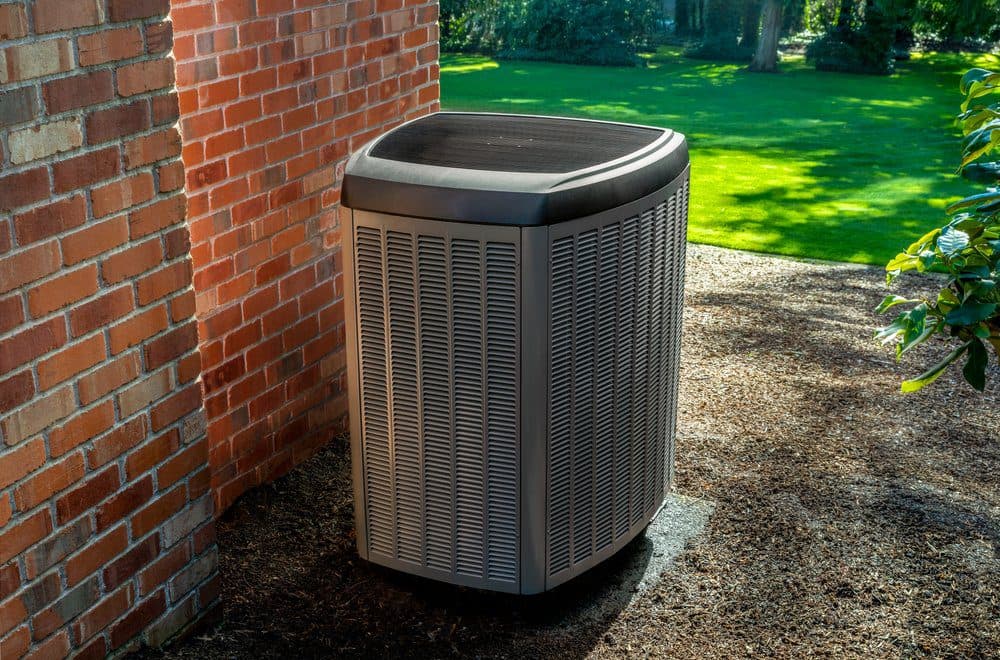 A gray air conditioner unit sitting outside of a brick house