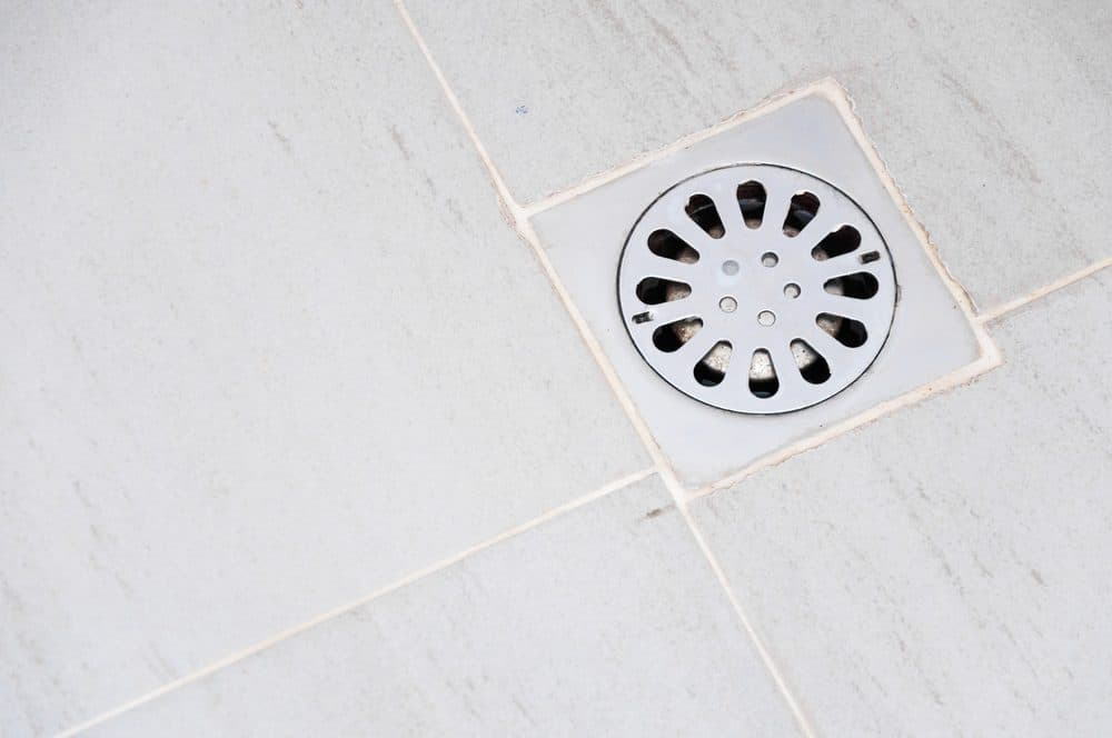 A circular floor drain nestled inside of a tiled floor