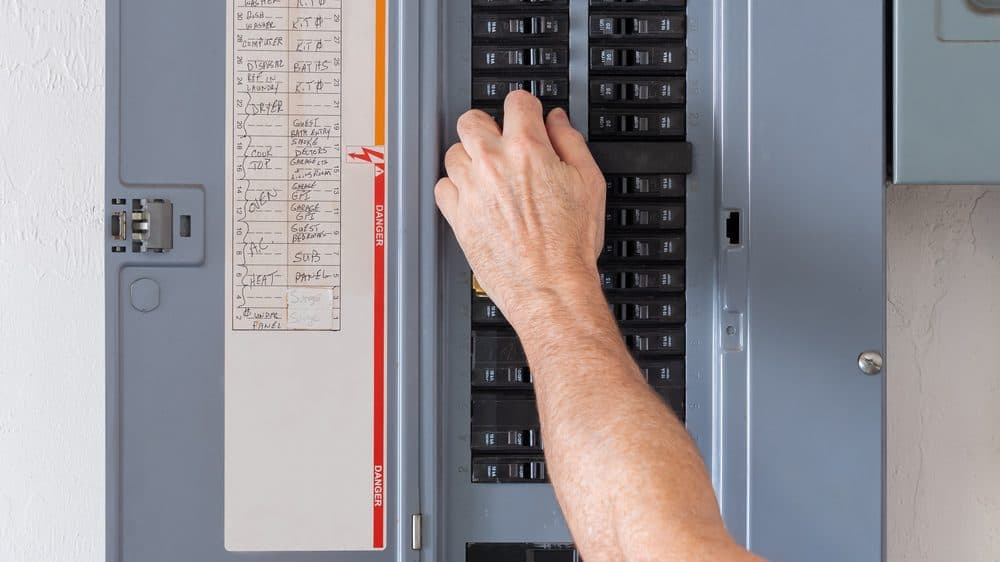 A man's hand flipping a breaker inside of a circuit breaker panel