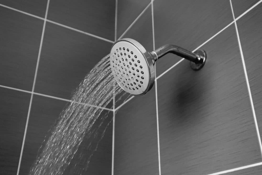 A shower head gushing water out of it inside of a gray tiled shower