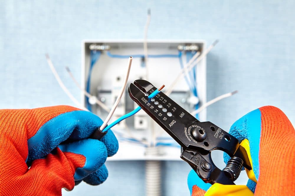 A technician wearing gloves using a wire tool to trim the coating off of a wire