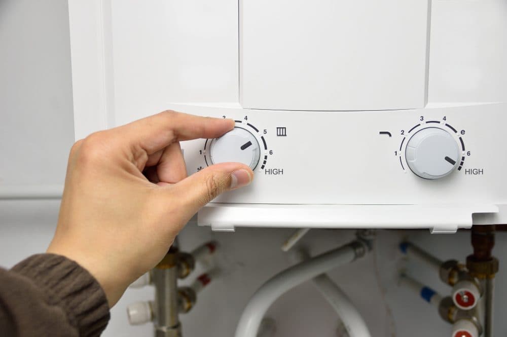 A hand adjusting the left knob of a tankless water heater