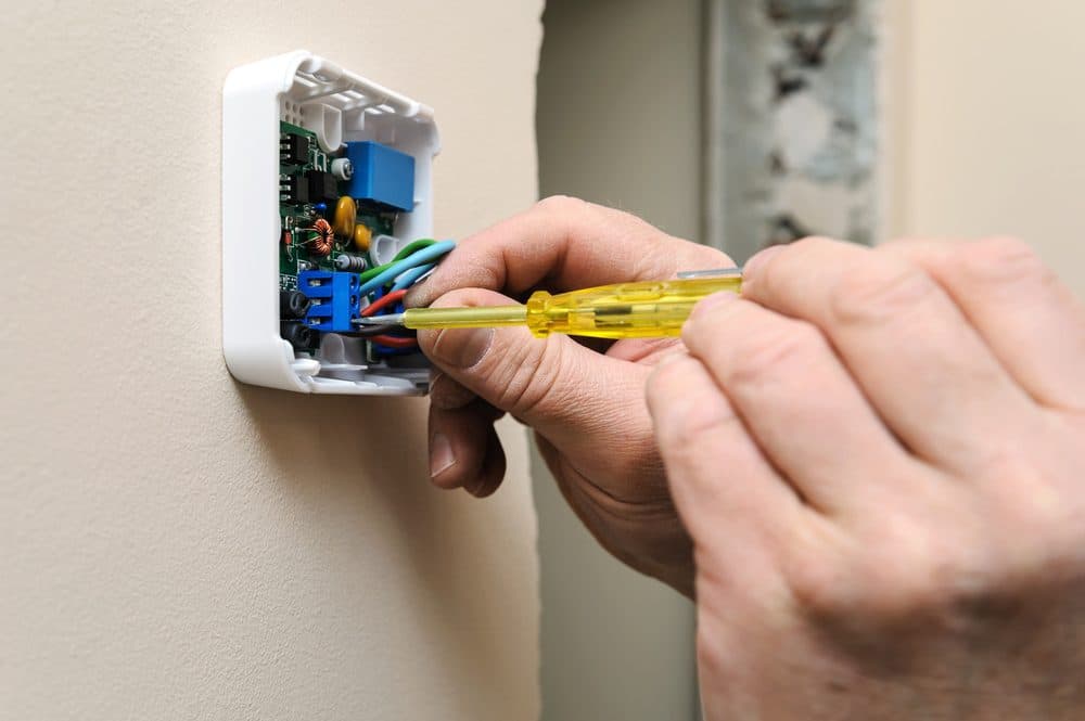 A hand using a screwdriver on the inside of an opened thermostat with the wires exposed