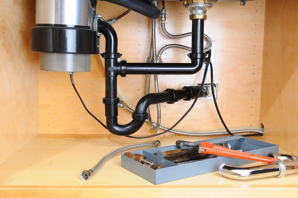 Tools sitting next to a garbage disposal that is being worked on inside of a kitchen cabinet