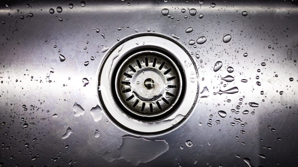 A kitchen sink drain with a light of splattering of water in the basin of the sink
