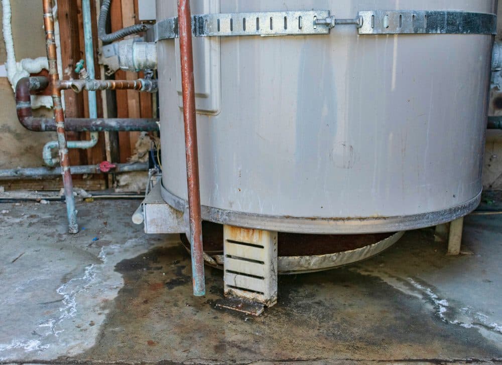 A large boiler system leaking water onto the floor in a house