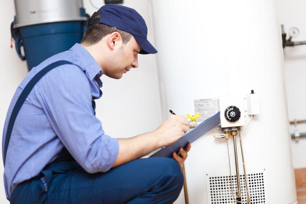 A Horizon technician on one knee writing onto a clipboard while replacing a water heater