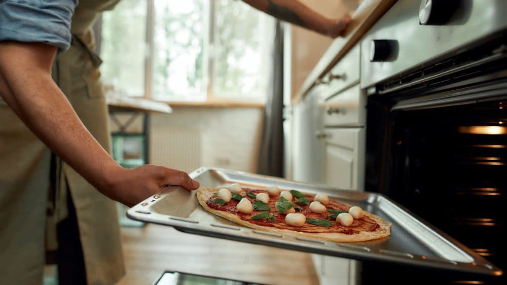 A cook placing a cheese and veggie pizza into the oven to cook