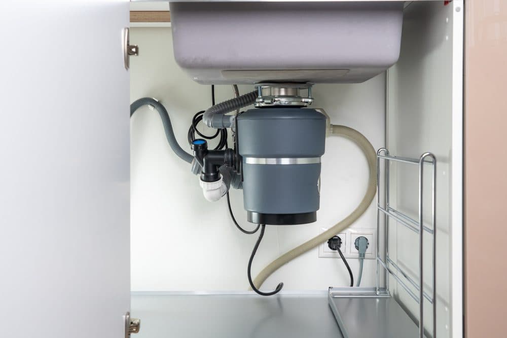 A garbage disposal inside of a cabinet underneath a kitchen sink