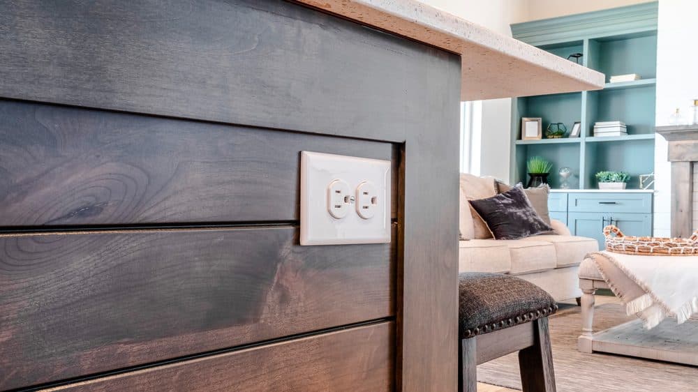 A three prong outlet installed horizontally on the side of a kitchen island covered in a wood material