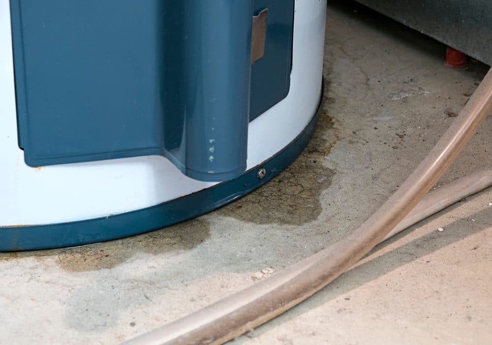 A water heater with dampness next to it showcasing signs of leaking onto a concrete floor