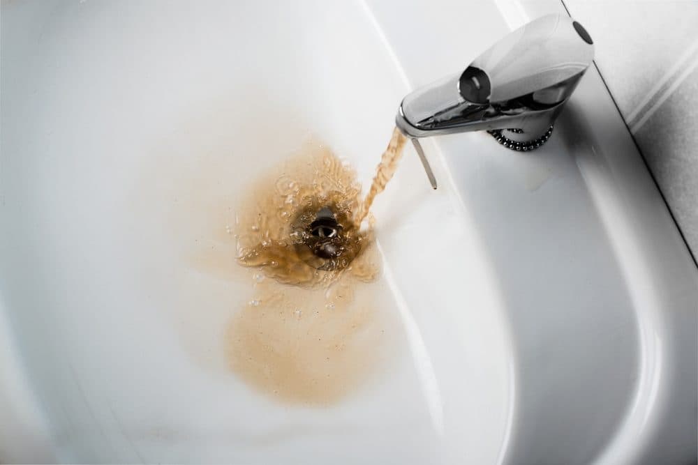 Dirty, brown colored water coming out of a sink faucet into a white sink