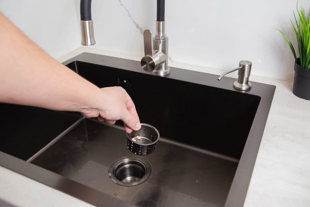 A kitchen strainer being raised out of the sink drain