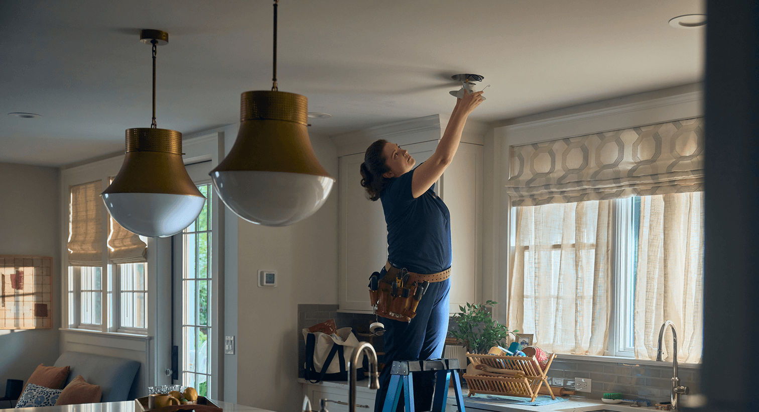 A professional electrician installing modern recessed ceiling lights during a residential kitchen electrical remodeling project.