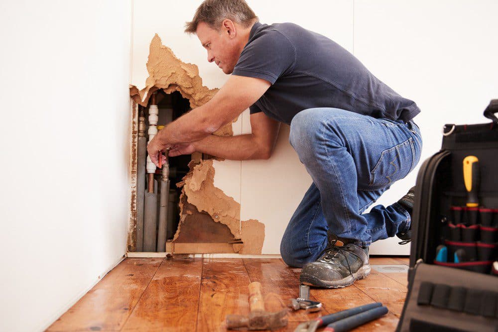 A Horizon technician on one knee next to an opening in the wall repairing a sewer pipe