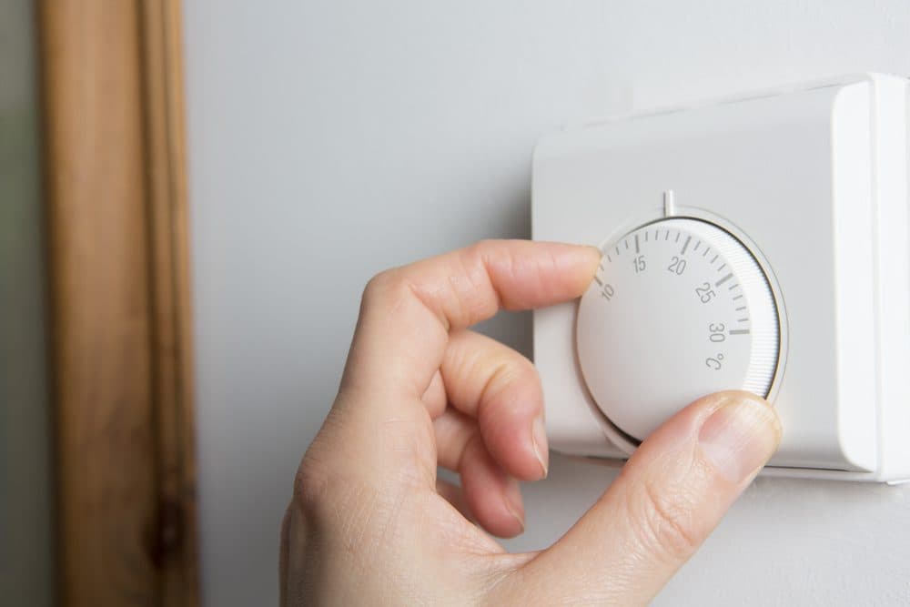 A hand adjusting the temperature knob on a traditional central heating thermostat